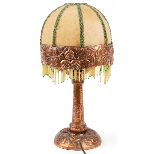 50 - Arts & Crafts copper table lamp decorated with stylized roses and tasselled shade, 49cm high