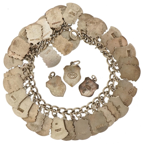 3435 - Silver charm bracelet with large collection of enamelled souvenir shield charms, 68.2g