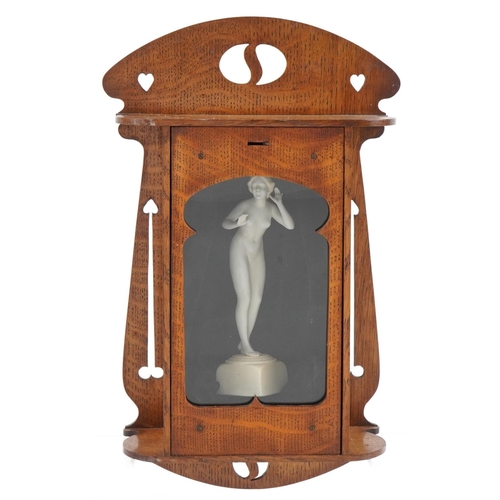 181 - Arts & Crafts oak wall hanging cabinet housing a bisque nude maiden figurine, 44cm high