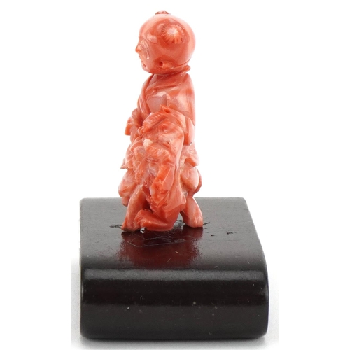 1211 - Chinese coral coloured okimono of a child on dog of Foo mounted on a wooden stand, 6cm in diameter