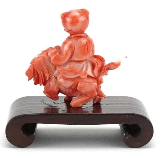 1211 - Chinese coral coloured okimono of a child on dog of Foo mounted on a wooden stand, 6cm in diameter