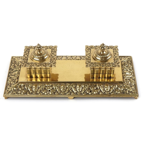 118 - Arts & Crafts brass double inkstand decorated with cherubs heads, 33cm wide