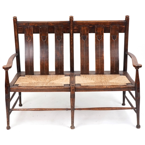 532 - Early 20th century Arts & Crafts oak two seat bench, probably by William Birch, the carved splat bac... 