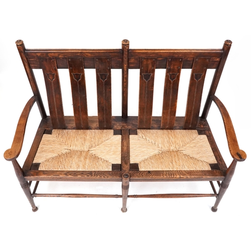 532 - Early 20th century Arts & Crafts oak two seat bench, probably by William Birch, the carved splat bac... 