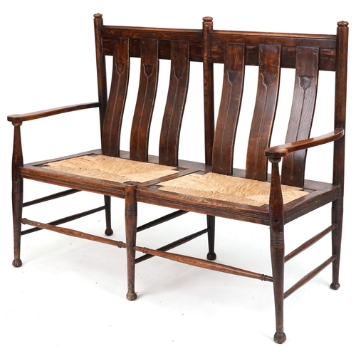 Early 20th century Arts & Crafts oak two seat bench, probably by William Birch, the carved splat backs raised on ring turned legs, 107cm H x 138cm W x 58cm D