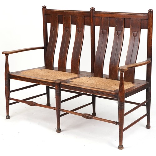 531 - Early 20th century Arts & Crafts oak two seat bench, probably by William Birch, the carved splat bac... 