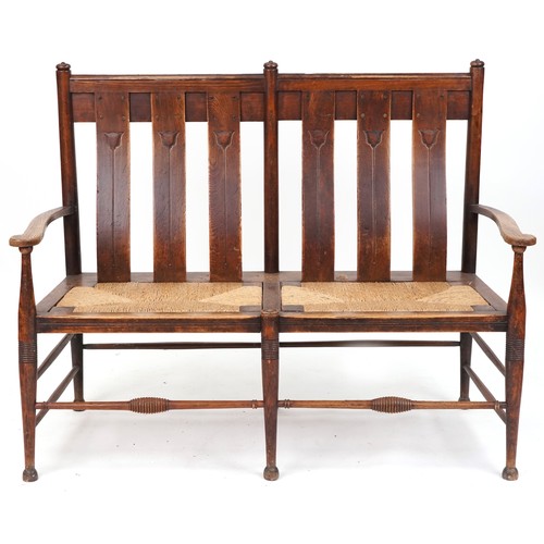 531 - Early 20th century Arts & Crafts oak two seat bench, probably by William Birch, the carved splat bac... 