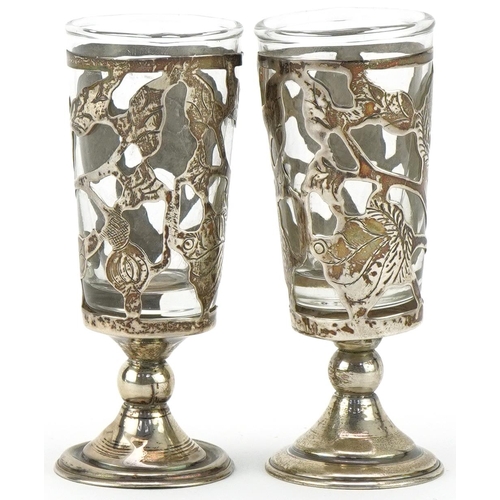 473 - Pair of sterling silver and moulded glass sherry glasses of pierced foliate design on circular stepp... 