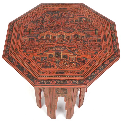 1021 - Late 19th century Burmese red lacquer octagonal folding table, the top profusely decorated with figu... 