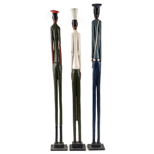 1392 - Three elongated carved wood figures comprising a police officer, an army officer and a chef, the lar... 