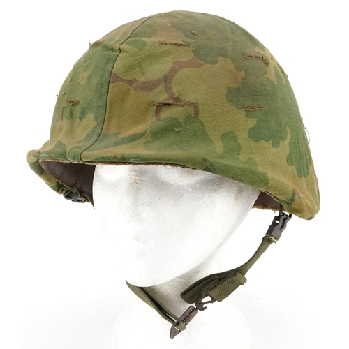 2599 - A military interest tin helmet with camo cover, liner and chin strap.