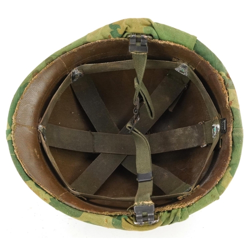 2599 - A military interest tin helmet with camo cover, liner and chin strap.