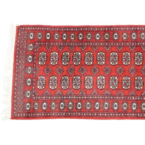 1033 - An Afghan runner, late 20th century, the red field with a two central rows of guls flanked by a comp... 