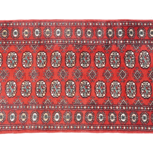 1033 - An Afghan runner, late 20th century, the red field with a two central rows of guls flanked by a comp... 