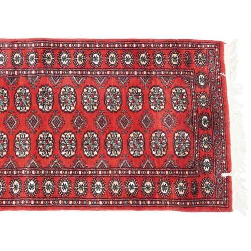 1033 - An Afghan runner, late 20th century, the red field with a two central rows of guls flanked by a comp... 