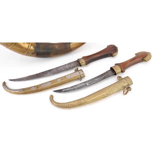 198 - Two similar Eastern curved blade daggers, each with hardwood handle and embossed brass scabbard toge... 