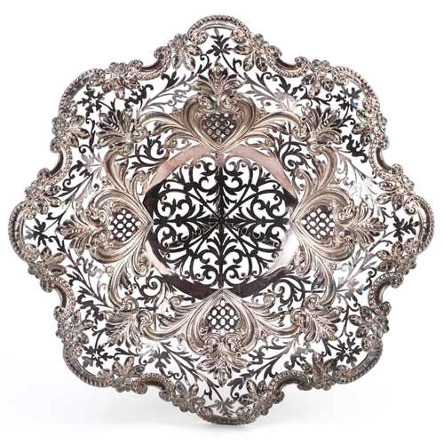 389 - An Edwardian silver centrepiece bowl, raised on three feet, profusely embossed and pierced with flow... 