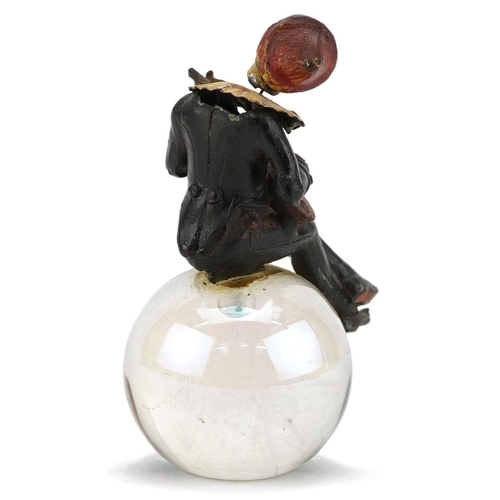 7 - A cold cast painted spelter nodding Pierrot seated on a globular glass ball, 10.5cm high.