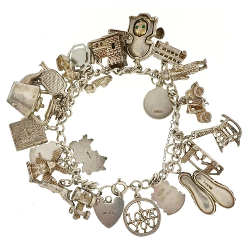 438 - A silver charm bracelet with a collection of mostly silver charms including Nelson, tractor and wind... 