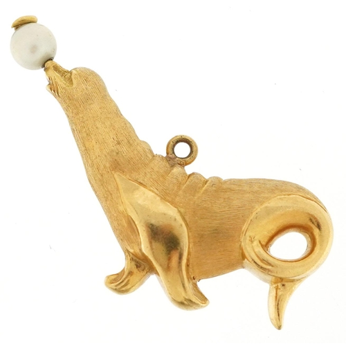 321 - A large unmarked gold charm in the form of a seal balancing a pearl ball, (tests as 9ct gold), 2.3cm... 