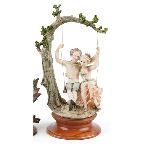 1297 - A Giuseppe Armani Capodimonte 'Lovers on a swing' porcelain figure group raised on a turned wood pli... 