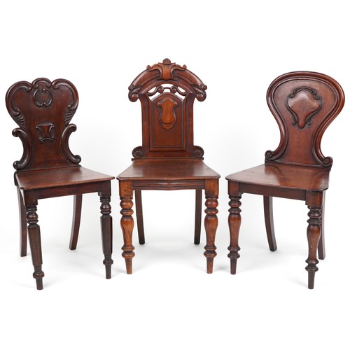 1025 - A group of three Victorian mahogany hall chairs, variously decorated, the largest 88cm high.