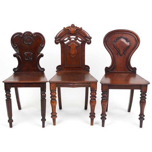 1025 - A group of three Victorian mahogany hall chairs, variously decorated, the largest 88cm high.