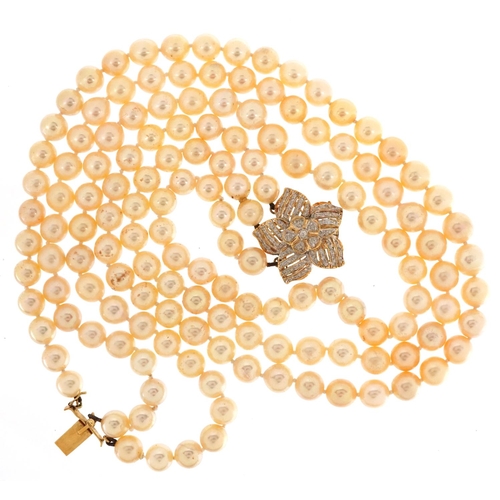 63 - A cultured pearl three row necklace with 18ct gold diamond set flower head clasp, each pearl approxi... 