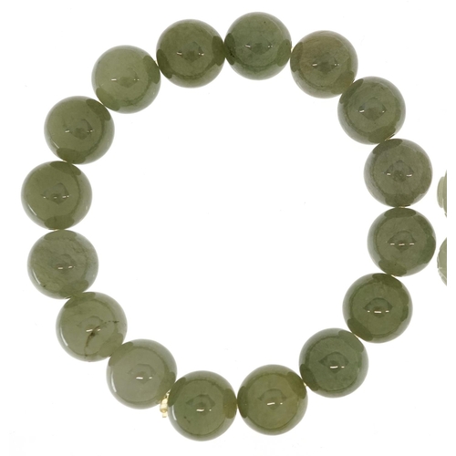 53 - Two Chinese jade bead bangles, one with carved decoration, the other spinach green.