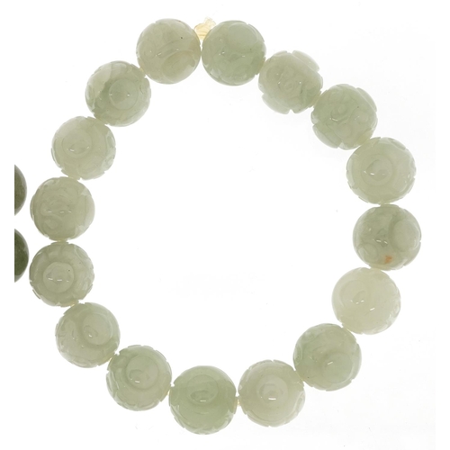 53 - Two Chinese jade bead bangles, one with carved decoration, the other spinach green.