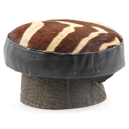 94 - An early 20th century African cowhide and leather footstool raised on an elephant skin covered base,... 