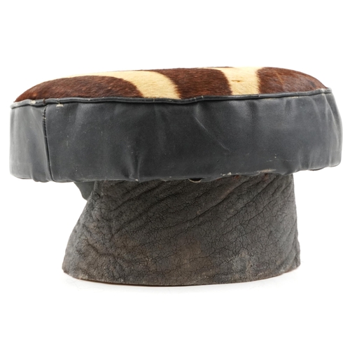 94 - An early 20th century African cowhide and leather footstool raised on an elephant skin covered base,... 