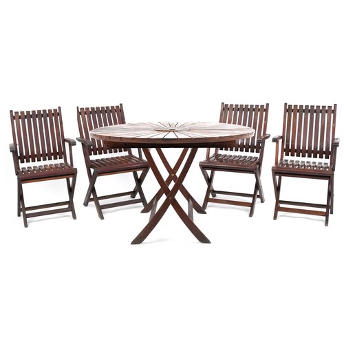 A 20th century circular teak garden table and four folding chairs together with a parasol and stand.