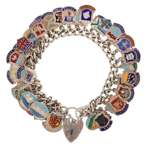 2065 - A silver charm bracelet with a large collection of silver and enamel souvenir shield charms, 80.8g.