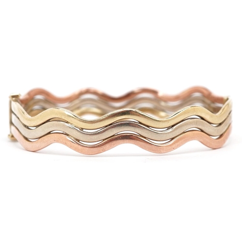 3008 - A 9ct three tone gold hinged bangle, 6cm in diameter, 14.4g.