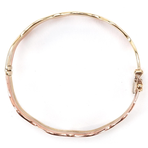 3008 - A 9ct three tone gold hinged bangle, 6cm in diameter, 14.4g.