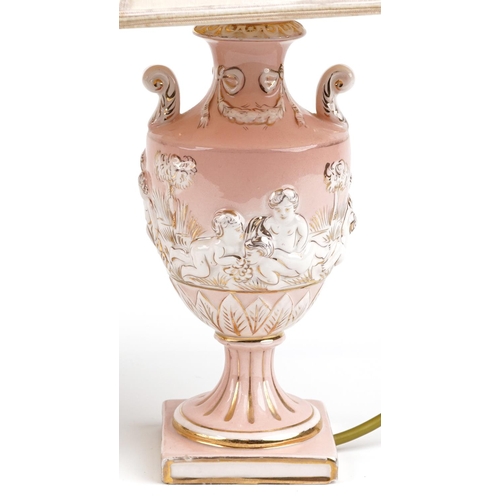 1173 - A pair of Italian porcelain table lamp bases, each modelled as a classical urn and decorated with Pu... 