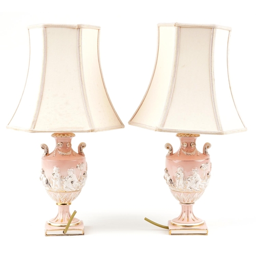 1173 - A pair of Italian porcelain table lamp bases, each modelled as a classical urn and decorated with Pu... 