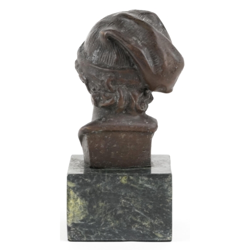 1115 - A patinated bronze head and shoulders bust of a young male wearing a hat, raised on a green marble b... 