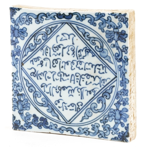 114 - An Islamic pottery tile hand painted with script amongst foliage, 19.5cm x 19.5cm.