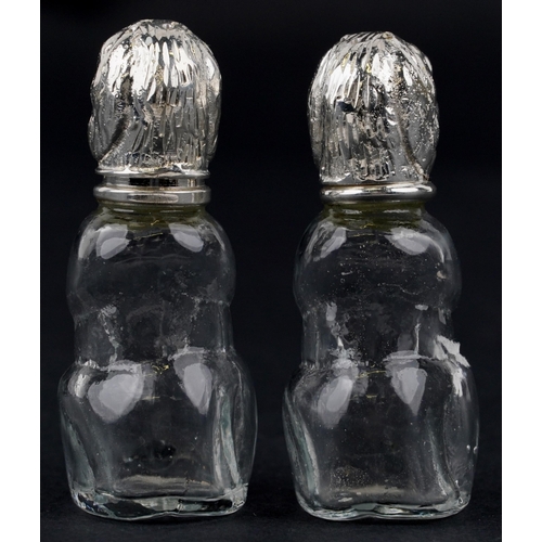 1087 - A pair of novelty glass salt and pepper casters with silver plated heads in the form of dogs, each 8... 