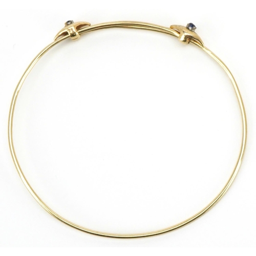 3105 - A 14ct gold adjustable bangle set with two sapphires, 6.5cm in diameter, 4.5g.