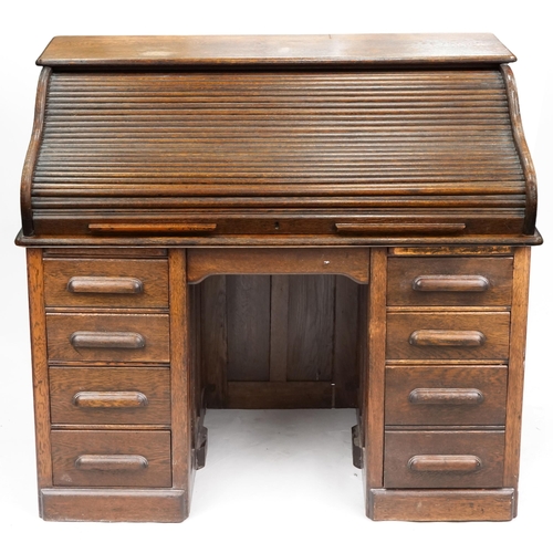 An early 20th century oak roll top desk the tambour front revealing a fitted interior above eight drawers, 114cm H x 127cm W x 76cm D.