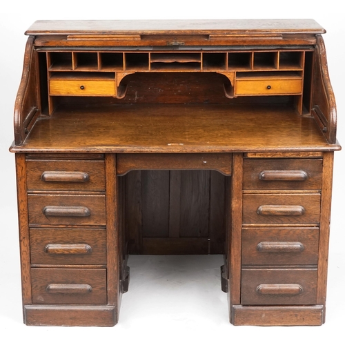 2056 - An early 20th century oak roll top desk the tambour front revealing a fitted interior above eight dr... 