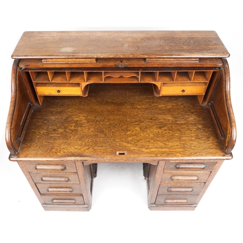 2056 - An early 20th century oak roll top desk the tambour front revealing a fitted interior above eight dr... 