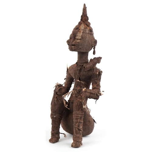 An African tribal carved softwood seated figure, possibly Benin, circa 1900, bound with string and feathers and covered with mud like clay, 49cm high.