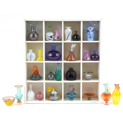 A good collection of Kosta Boda miniature art glass vases, bowls, bottles and figures, various artists and designs, the majority signed to the base, the largest 13cm high, together with a Kosta Boda wall hanging display shelf.