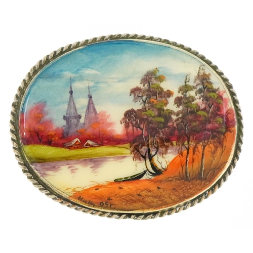 3040 - A vintage white metal brooch hand painted with a river before a church, indistinctly signed, 5cm wid... 