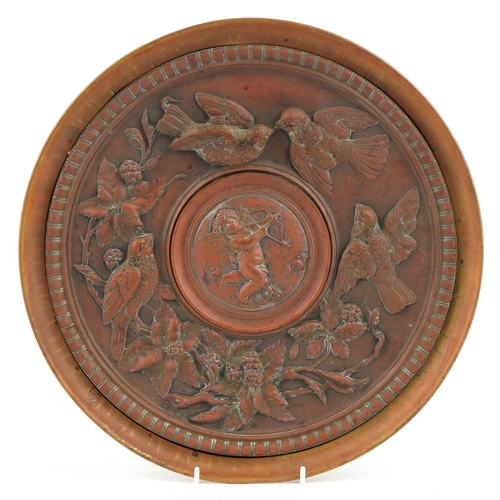 397 - An Arts & Crafts brass and copper circular embossed panel, the centre decorated with Cupid surrounde... 