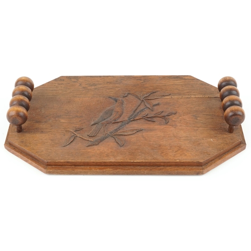 398 - An Arts & Crafts oak canted rectangular tray, the top carved with a bird, fitted with two bobbin tur... 